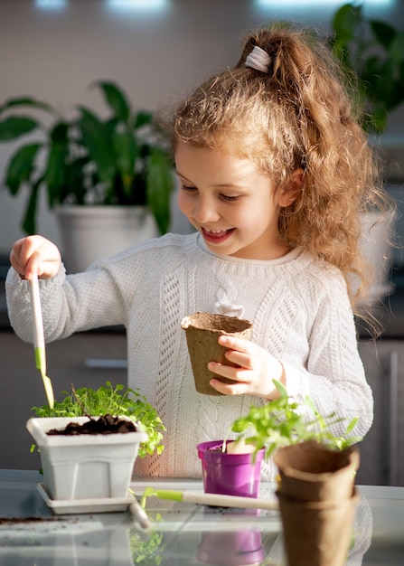 Una ragazza carina pianta a casa in vasi ecologici Indossa un maglione bianco Il giardino di casa Hobby