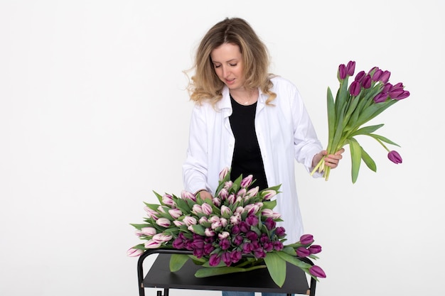 Una ragazza carina prende un tulipano viola dal tavolo per un bouquet Si erge su uno sfondo bianco