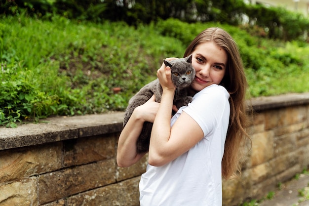una ragazza carina tiene in braccio un gatto grigio mentre è fuori nella natura ragazza con un gatto e un carrie