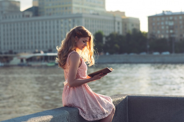 Una ragazza che legge un libro sulla sponda del fiume.