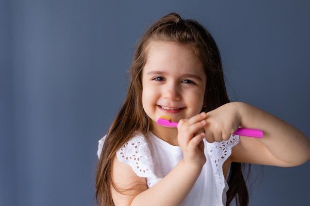 Una ragazza che si lava i denti con uno spazzolino rosa.