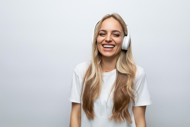 Una ragazza con entusiasmo e gioia sul viso ascolta musica in grandi cuffie bianche su un bianco