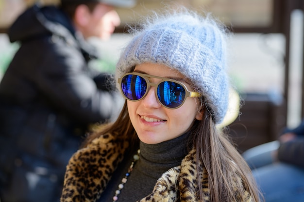 Una ragazza con gli occhiali blu e un cappello grigio grassoccio caldo in posa fuori nella stagione fredda. Ritratto di una bella ragazza con gli occhiali