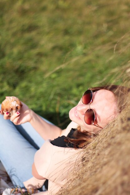 una ragazza con gli occhiali scuri beve caffè con un muffin