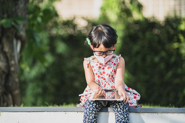 Una ragazza con gli occhiali siede su un muro con un tablet tra le mani.