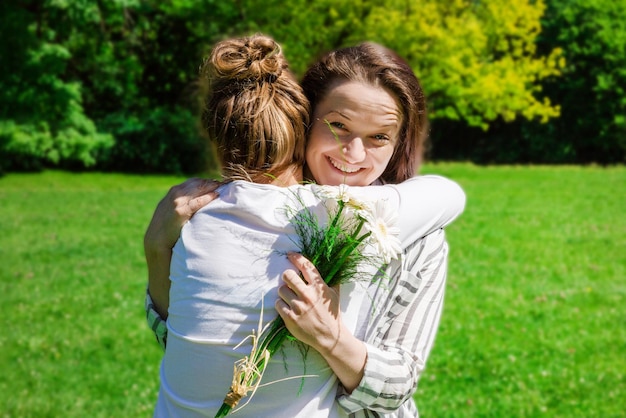 Una ragazza con i capelli biondi pettinati in uno chignon regala a sua madre un mazzo di fiori bianchi