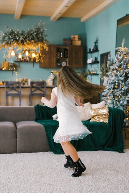 Una ragazza con i capelli lunghi e un vestito bianco gira in soggiorno con un albero di Natale