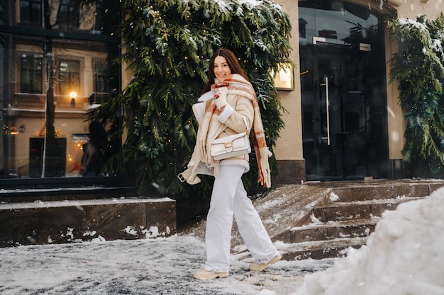 Una ragazza con i capelli lunghi in una sciarpa e con una borsetta bianca cammina per strada in inverno