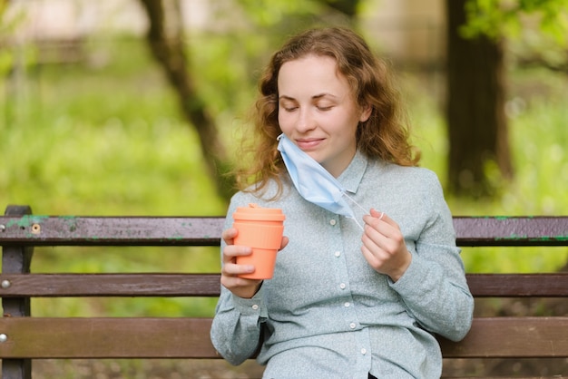 Una ragazza con i capelli ricci rimuove una maschera per bere il caffè