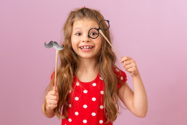 Una ragazza con i capelli ricci tiene un bel paio di baffi e occhiali su un bastone.