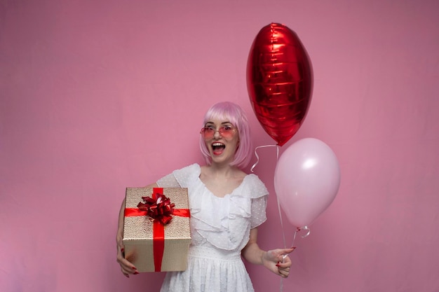 una ragazza con i capelli rosa tiene palloncini e regali e celebra un compleanno donna con regali