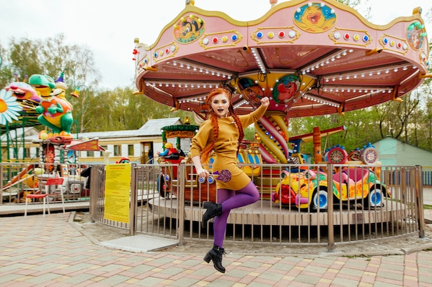 Una ragazza con i capelli rossi cammina e si diverte in un parco divertimenti, con in mano una lecca-lecca.