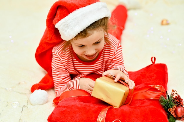 Una ragazza con il cappello rosso di Babbo Natale e rosso sul letto con un regalo Preparazione per la celebrazione del nuovo anno