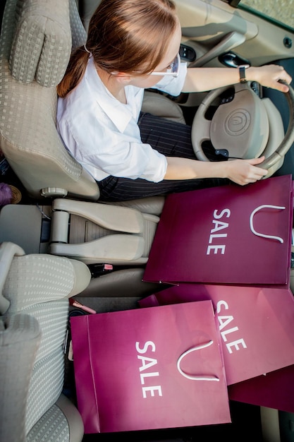 Una ragazza con le borse della spesa sta guidando un concetto di auto di sconti e vista dall'alto dello shopping