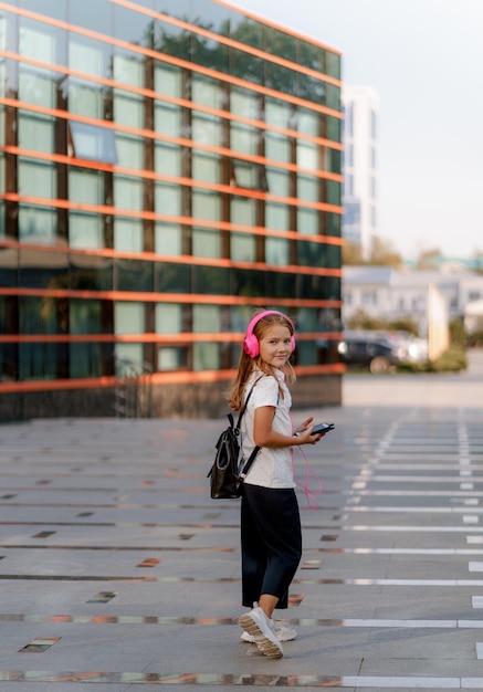 una ragazza con le cuffie rosa e con uno zaino passeggia per la città