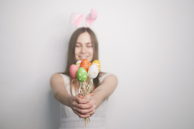 Una ragazza con le orecchie di coniglio nelle sue mani tiene le uova di pasqua su uno sfondo bianco il concetto di pasqua