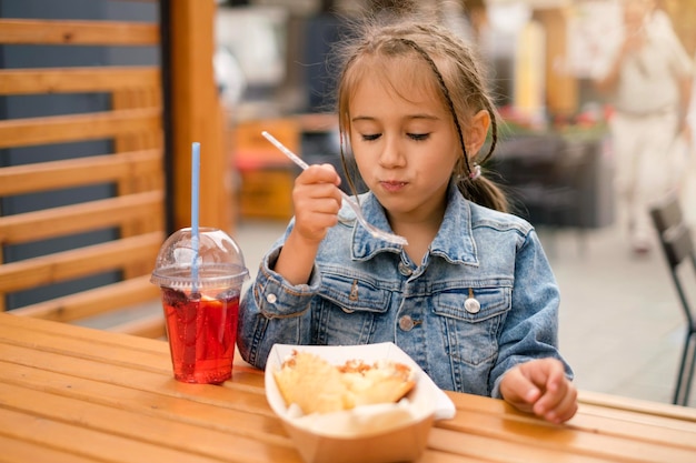 Una ragazza con le trecce si siede al tavolo di un ristorante e mangia con il piacere del cibo da asporto