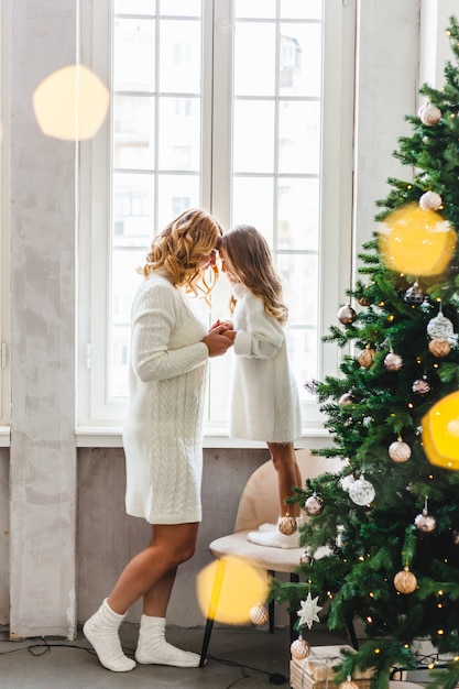 Una ragazza con sua madre vicino all'albero di Natale, l'interno decorato per il nuovo anno e il Natale, la famiglia e la gioia, le tradizioni