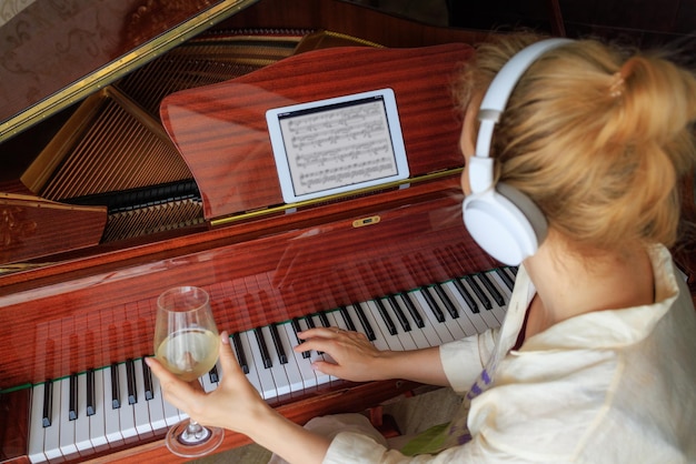 Una ragazza con un bicchiere di vino è seduta vicino al pianoforte Il concetto di solitudine