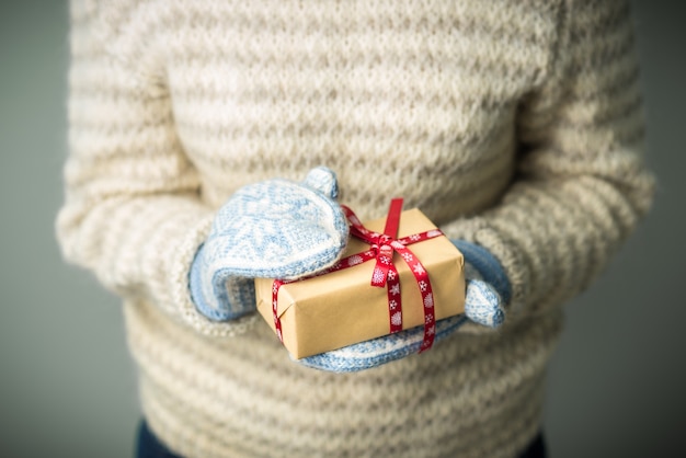 Una ragazza con un caldo maglione lavorato a maglia e guanti è in possesso di un regalo di Natale.