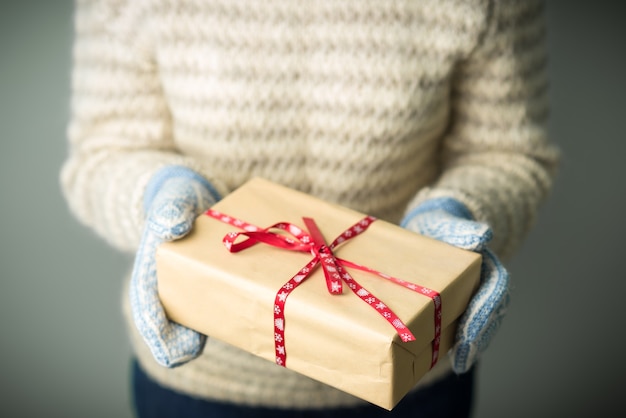 Una ragazza con un caldo maglione lavorato a maglia e guanti è in possesso di un regalo di Natale.