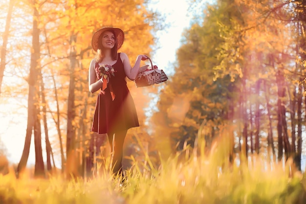 Una ragazza con un cappello durante una passeggiata nel parco. Una ragazza con un cesto cammina in autunno. La ragazza sta camminando lungo la strada al tramonto.