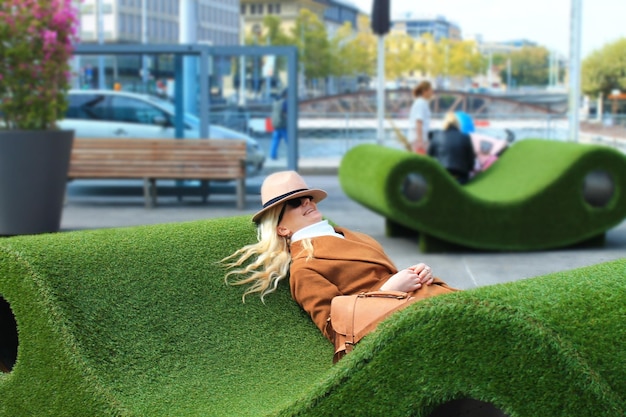 Una ragazza con un cappello e un cappotto marrone giace e riposa sull'erba La bionda a Ginevra in Svizzera