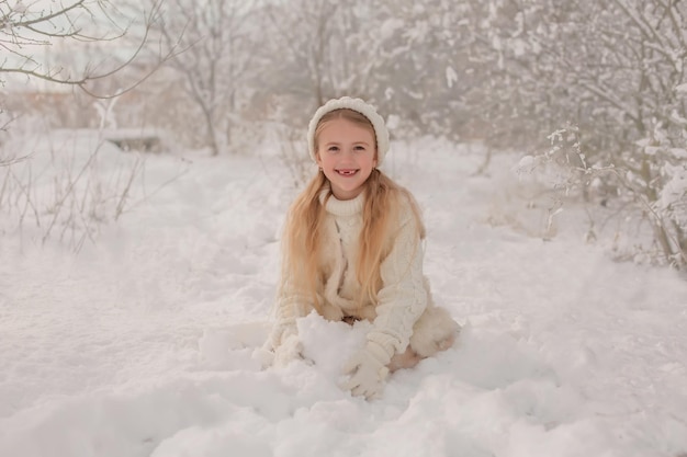 una ragazza con un cappello e un maglione lavorati a maglia bianchi scolpisce la neve innevata nel parco