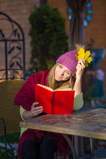 una ragazza con un cappello e un maglione si siede a un tavolo in un bar e legge un libro