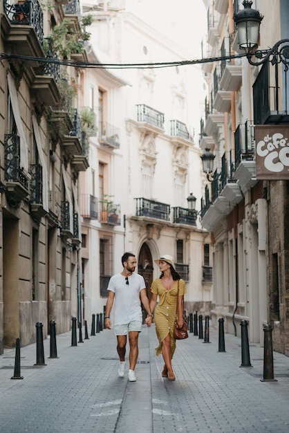 Una ragazza con un cappello e un vestito giallo con una profonda scollatura e il suo ragazzo con la barba camminano e si fissano nella vecchia città della Spagna. Un paio di turisti ad un appuntamento a Valencia.