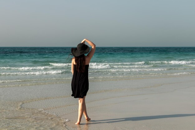 Una ragazza con un cappello e un vestito neri si trova sullo sfondo del mare