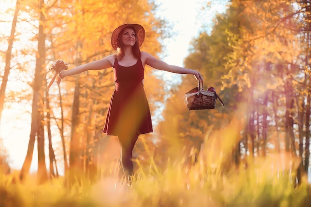 Una ragazza con un cappello mentre passeggia nel parco Una ragazza con un cesto cammina in autunno Una ragazza cammina lungo la strada al tramonto