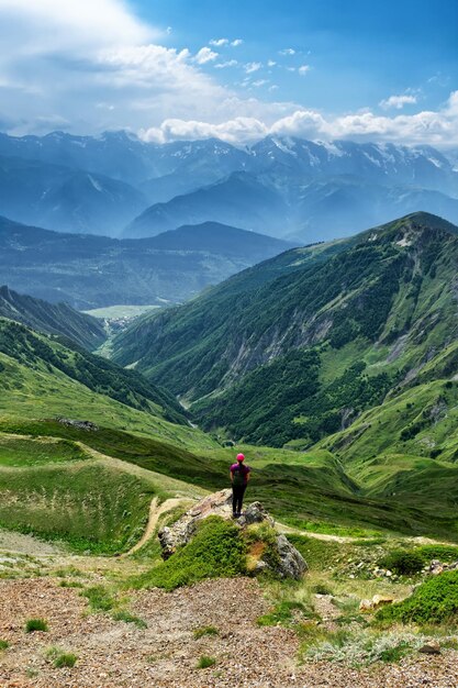 Una ragazza con un cappello si erge su una pietra sullo sfondo delle montagne del Caucaso Svaneti in estate