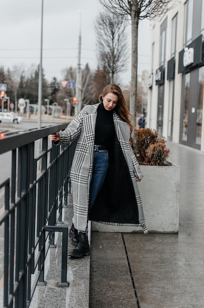 una ragazza con un cappotto grigio e jeans si aggrappa al corrimano