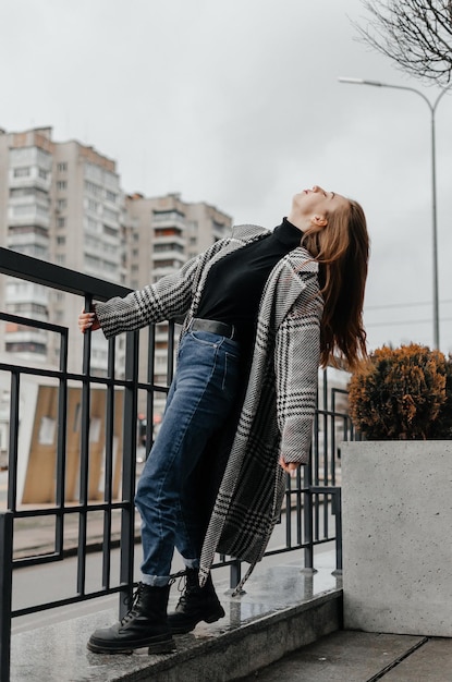 una ragazza con un cappotto grigio e jeans si aggrappa al corrimano