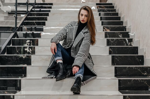 una ragazza con un cappotto si siede sulle scale