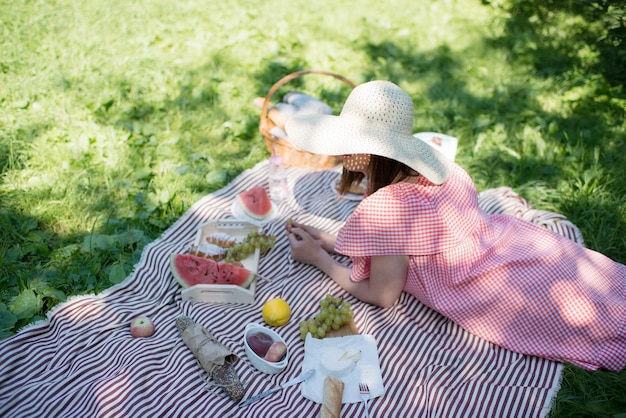 Una ragazza con un grande cappello di paglia è sdraiata sulla spiaggia, durante un picnic.