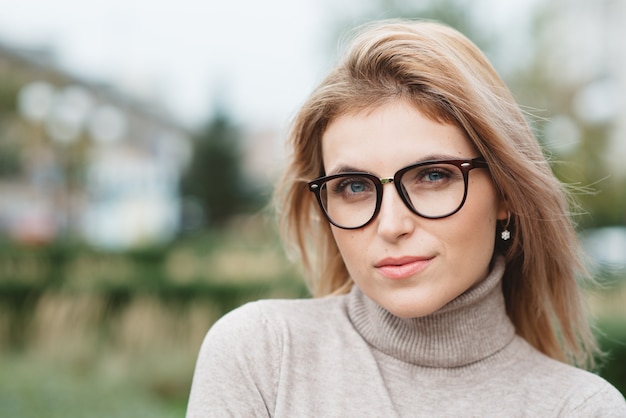 Una ragazza con un maglione beige, occhiali alla moda e orecchini