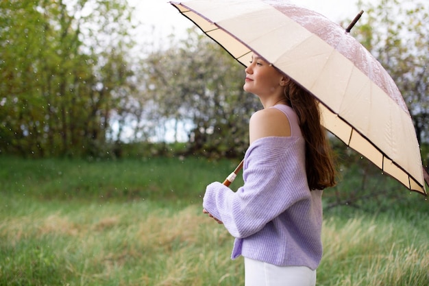 Una ragazza con un maglione è in piedi sotto un ombrello piove