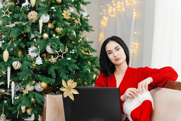 Una ragazza con un maglione rosso con un laptop seduto e guardando dritto nella ricerca del sito della telecamera