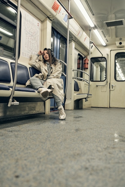 Una ragazza con un trench beige viaggia in un vagone della metropolitana.