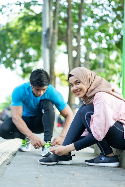 Una ragazza con un velo sorridente si aggiusta i lacci delle scarpe prima di fare jogging all'aperto nel parco