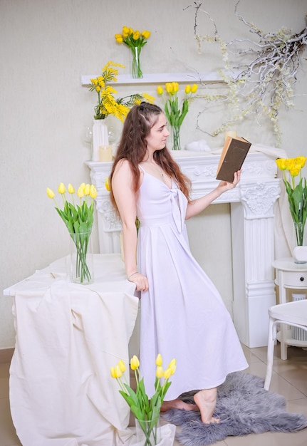 Una ragazza con un vestito bianco e i capelli lunghi legge un libro sullo sfondo di fiori gialli