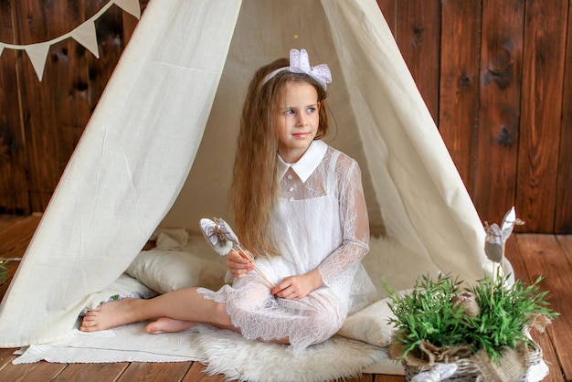 Una ragazza con un vestito bianco è seduta in una tenda wigwam