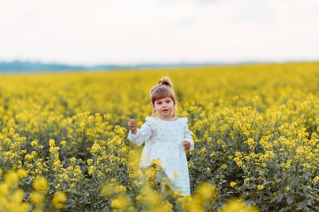 una ragazza con un vestito bianco in un campo di colza gialla