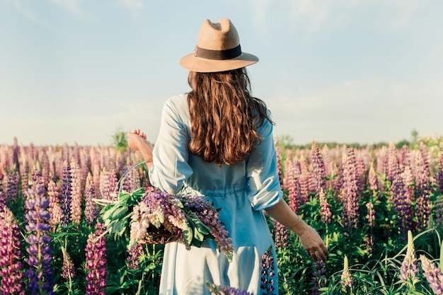 Una ragazza con un vestito blu su un campo viola di lupini. Prato con fiori viola in estate.