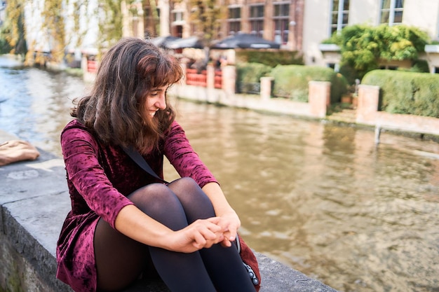 una ragazza con un vestito di corduroy rosso con la schiena aperta cammina per le strade di Bruges in un giorno d'autunno