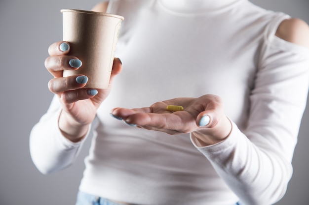 Una ragazza con un vestito giallo tiene una pillola e un bicchiere d'acqua