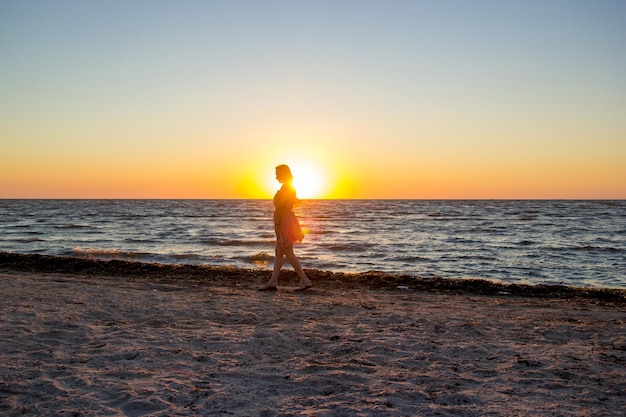 Una ragazza con un vestito rosa cammina lungo una spiaggia deserta all'alba