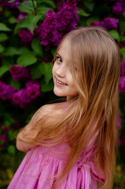 Una ragazza con un vestito rosa si trova davanti a dei fiori viola.